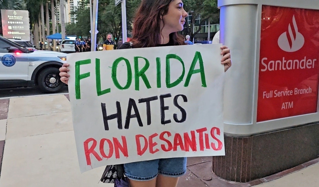 A woman protests outside of a Ron DeSantis donor event in Miami.