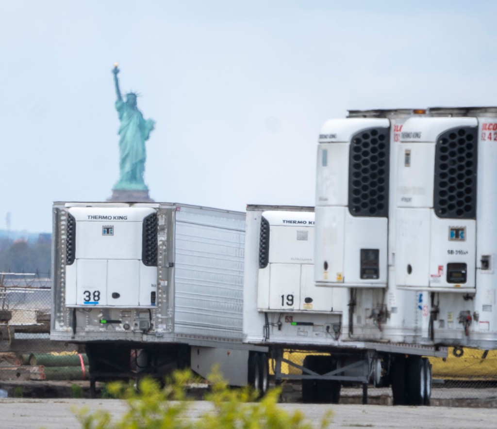 Refrigerated trucks and Statue of Liberty in Background, with victims of Covid-19, kept at Industry City in Brooklyn, New York on May 9th, 2020.