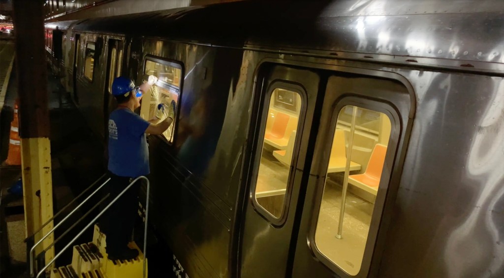 A worker on a ladder repairs a broken window on subway car