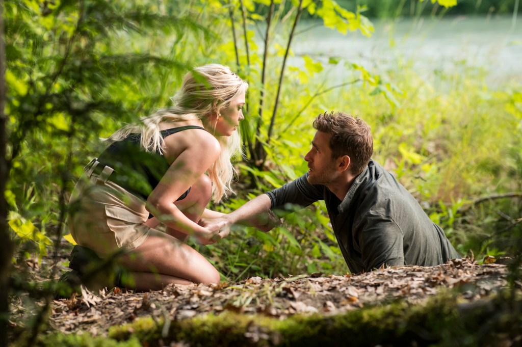 Will (Oliver Jackson Cohen) and his affair partner, Cara (Ashley Benson) looking at each other crouching over a log in the woods. 